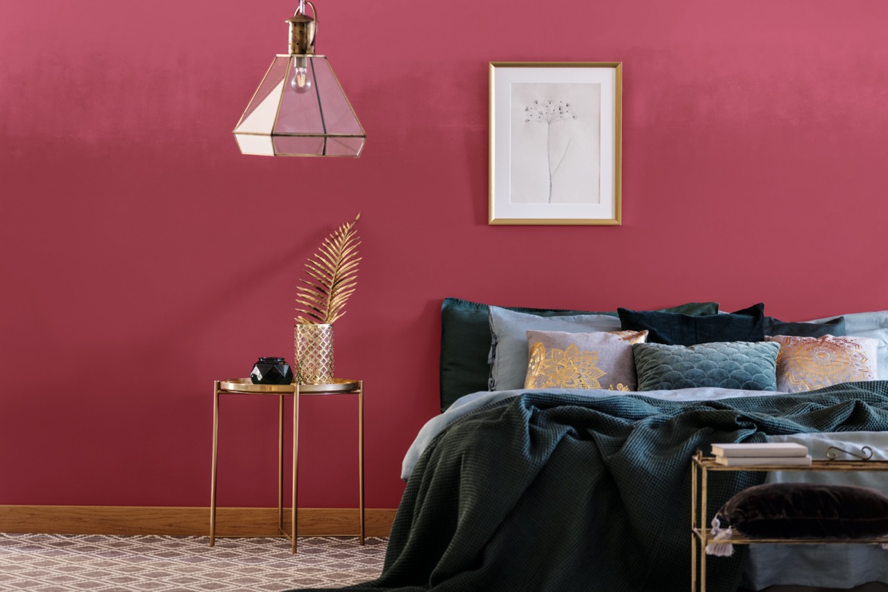 Emerald green bed against red wall with poster in bedroom interior with lamp above gold table; Shutterstock ID 1090095470; purchase_order: 10580; job: Calendario; client: Sinteplast; other: Sinteplast
